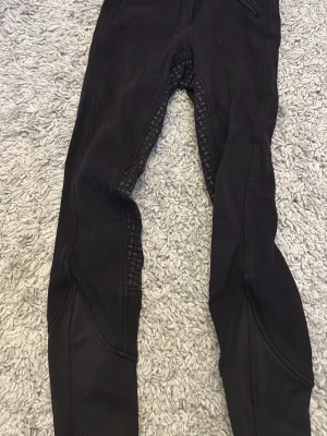 Svarta ridleggings från CRW - Svarta ridleggings från CRW med helskodd silikongrepp på insidan av benen och sätet. Stretchigt material som ger bra rörelsefrihet och bekväm passform. Perfekta för ridning och träning, med diskret logga vid linningen.