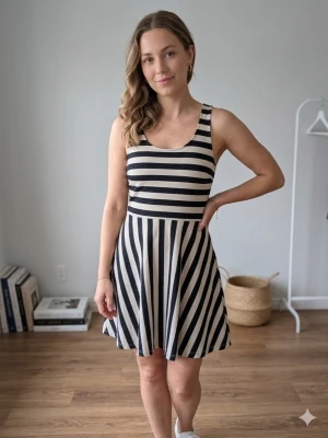 Randig kortklänning med korsade band - Snygg kortklänning med svart och vita ränder. Klänningen har ärmlös design och korsade band i ryggen som ger en cool detalj. Den har en rundad halsringning och ett lätt utsvängt fall. Perfekt för dig som gillar en stilren look.