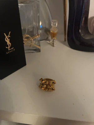 Guldig statementring med nitar - Cool och chunky ring i guldmetall med flera små nitar som ger en edgy vibe. Perfekt accessoar för dig som vill sticka ut och addera lite attityd till din stil. Ringen har en bred design och glänsande finish.