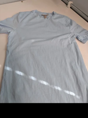 Ljusblå slim fit t-shirt från H&M - En stilren ljusblå t-shirt från H&M i slim fit-modell. Tillverkad i mjuk bomull och har klassisk rund halsringning och korta ärmar. Perfekt basplagg för en enkel och fräsch look.