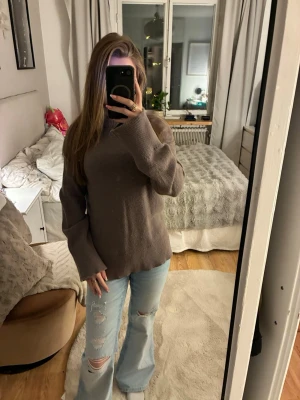 Brun stickad tröja med hög krage - En enkel och stilren brun stickad tröja med hög krage och långa ärmar. Tröjan har en rak passform och ribbstickade muddar vid ärmslut och nederkant. Perfekt att matcha med jeans för en avslappnad look.