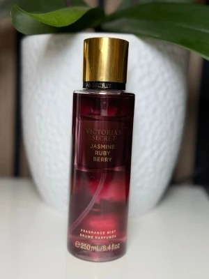 Mörkröd parfymflaska med guldkork - Snygg parfymflaska från Victoria's Secret i mörkröd glas med elegant guldfärgad kork. Flaskan har en stilren och modern design som passar perfekt på sminkbordet. Märket syns tydligt på flaskans hals.