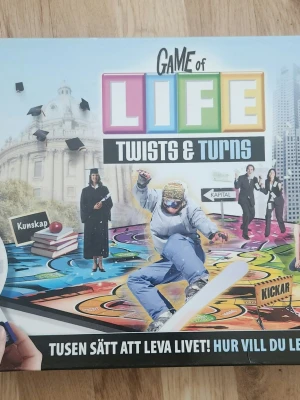 Game of Life Twists & Turns brädspel - Game of Life Twists & Turns är ett färgglatt brädspel från Hasbro där du utforskar olika livsval och utmaningar. Spelet har en modern design med livfulla färger och inkluderar spelbräda, kort och tillbehör. Perfekt för familj eller vänner som gillar strategiska och roliga spel.
