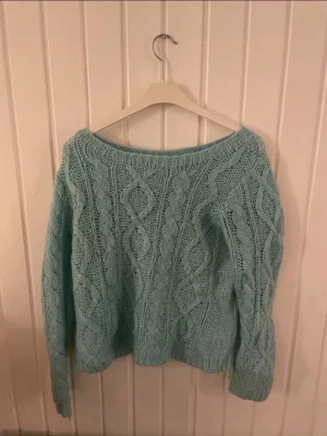 Ljusblå kabelstickad tröja H&M - Mysig ljusblå stickad tröja från H&M med kabelstickat mönster och bred rund halsringning. Tröjan har långa ärmar och ribbade muddar vid ärmslut och nederkant. Perfekt för kyliga dagar och enkel att styla till jeans eller kjol.
