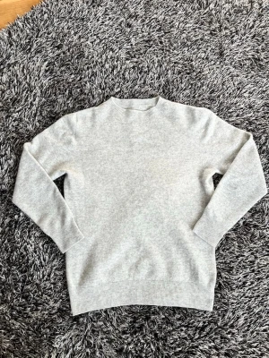 Ljusgrå stickad tröja i kashmir  - En stilren ljusgrå stickad tröja med rund halsringning och långa ärmar. Tröjan har ribbade muddar vid ärmslut och nederkant. Perfekt för lager på lager och enkel att matcha med olika outfits. Tröjan är köpt på Plick och har inget märke.  Men är i toppskick. Pris ej hugget i sten. 