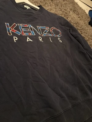 Mörkblå Kenzo sweatshirt - Säljer en mörkblå sweatshirt från Kenzo med stort broderat Kenzo Paris-tryck i färgglada detaljer på bröstet. Tröjan har rund halsringning och ribbade muddar. Perfekt för dig som gillar streetwear och vill sticka ut lite extra.