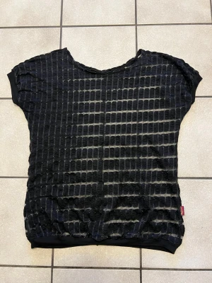 Svart transparent topp med struktur storlek M/L - Cool svart topp med transparent rutmönster och strukturerad yta. Oversize passform och korta ärmar. Perfekt att styla lager på lager för en edgy look.