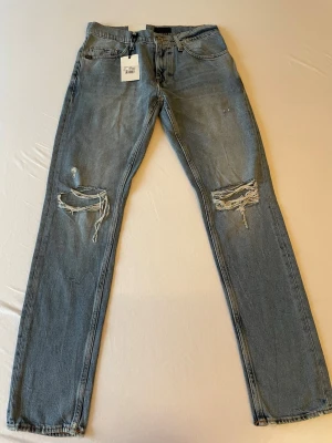 Oanvända Tiger of Sweden jeans  - Säljer ett par blå jeans med raka ben och slitningar samt hål på båda knäna. Modellen är Pistolero med straight leg. Storlek 29/32. Nypris är 1599.