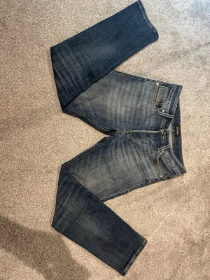 Mörkblå jeans från Jack & Jones, storlek 28/30 - Snygga mörkblå jeans från jack & Jones med klassisk femficksmodell och subtila slitningar på låren. Jeansen har normal midja, dragkedjegylf och är tillverkade i mjuk denim med lite stretch för extra komfort.
