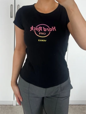 Topp - Svart topp från Hard Rock Cafe Venice med tryck i rosa och gult framtill. Modellen är figurnära med rund hals och korta ärmar. Tillverkad i 100% bomull. Storlek L, tror det är barnstorlek, jag har XS/S och den passar mig 🖤