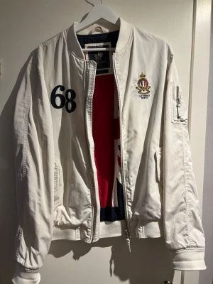 Morris jacka - Snygg vit bomberjacka från Morris Gents med broderad logga på bröstet och siffran 68 på ena sidan. Jackan har dragkedja, fickor och ribbade muddar. Perfekt för dig som vill ha en stilren och sportig look.