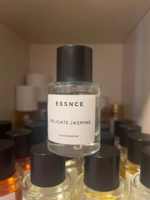 ESSNCE Delicate Jasmine parfym - Minimalistisk parfymflaska från ESSNCE med doften Delicate Jasmine. Flaskan är genomskinlig i glas med svart cylinderformad kork och vit etikett med svart text. Eau de Parfum som ger en fräsch och blommig jasminupplevelse.
