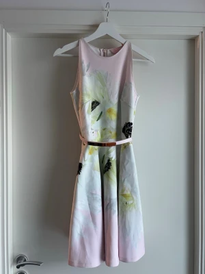 Ljusrosa blommig kortklänning Ted Baker - Söt Ted Baker ljusrosa kortklänning med blommigt mönster i vitt, gult och svart. Klänningen har ärmlös design, rund halsringning och ett smalt bälte i midjan som markerar siluetten. Perfekt för sommarens alla tillfällen. Storlek 0 motsvar XS. 
