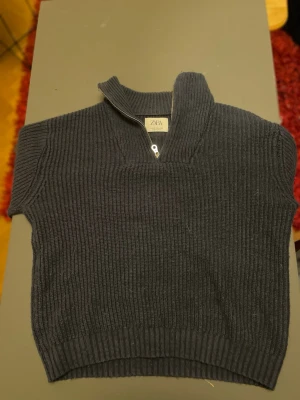Mörkblå stickad tröja från Zara - Säljer en mörkblå stickad tröja från Zara med korta ärmar och halv dragkedja vid halsen. Tröjan har ribbstickad struktur och hög krage som kan vikas ner. Perfekt för lager på lager och en snygg casual look.