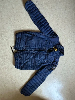 Mörkblå dunjacka från PJS - Snygg mörkblå dunjacka från Parajumpers. Jackan har quiltad design, hög krage och dragkedja framtill. Perfekt för kalla vinterdagar och har praktiska fickor med dragkedja