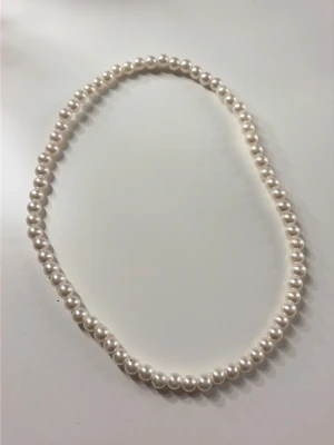 Klassiskt pärlhalsband i vitt - Snyggt halsband med vita, runda pärlor som ger en tidlös och elegant look. Perfekt för dig som gillar stilrena accessoarer. Halsbandet har en enkel design utan synligt lås och pärlorna är jämnt stora och blanka.