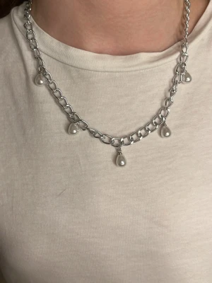Silverfärgat halsband med pärlor - Snyggt halsband i silverfärgad metall med fem hängande vita pärlor. Kedjan har en chunky design den är 40-45cm och justerbar!