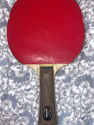 Yasaka pingisracket röd gummi - Ny pris:1600kr .Pingisracket från Yasaka med rött gummi och trähandtag. Handtaget har en mörk träfinish och en svart detalj med texten 'Sweden Classic'. Gummit är fastklistrat på nästan hela racket bara loss på 2 bilden men går att laga enkelt genom att limma.