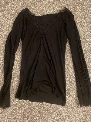 Svart långärmad topp med spets - Svart långärmad topp från Intimissimi med v-ringning och fina spetsdetaljer vid halsen. Tillverkad i en mjuk blandning med kashmir som känns lyxig och skön mot huden. Perfekt för dig som gillar stilrena och feminina plagg. Har ett litet litet hål som endast syns om du strechar ut tröjan,