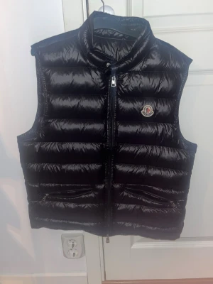 Moncler Gui - Moncler Gui väst, skick 10/10, storlek M, köpt 2022,moncler påsen man ska lägga västen i följer också med. Kan skicka fler bilder osv om ni vill legitcheka, skriv vid frågor eller funderingar, 