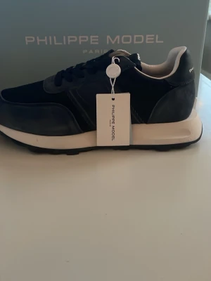 Philippe Model svarta sneakers - Stilrena svarta sneakers från Philippe Model med vita detaljer och tjock vit sula. Ovandelen är i en mix av mocka och textil, med snygga sömmar och logga på hälen. Aldrig använda och köpta på Philippe Models hemsida, bevis och kvitto finns. Allt originellt medföljer. Kan skickas, finns annars att hämta och prova i Mariefred. Ca 2200 kr nypris.