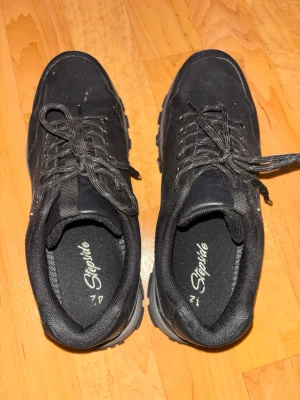 Svarta sneakers från Stepvite - Säljer ett par svarta sneakers från Stepvite med robust sula och klassisk låg profil. Skorna har svarta snören, metallöljetter och diskret logga på innersulan. Ovandelen är i textil och syntetmaterial, perfekt för en clean och enkel look. Använda en gång! 🩷