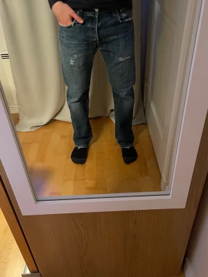 Levi's 501 - Säljer ett par blå Levis 501:or med snygga slitningar och raka ben. Jeansen har klassisk femficksdesign och en snygg tvättad look. Materialet är denim. Skicket är satt som acceptabelt pga slitningarna som enligt mig gör de snyggare :) Storlek: W30 L30                            Ställ frågor vid funderingar. 