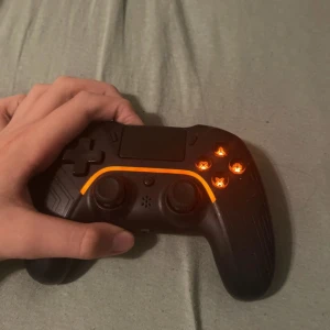 Svart trådlös spelkontroll ps4 - Snygg svart handkontroll med LED-belysning runt knapparna och touchpad upptill. Kontrollern har två analoga spakar, styrkors och fyra knappar på höger sida. Ergonomisk form och mönstrad yta för bättre grepp. Perfekt för gaming på konsol eller PC.