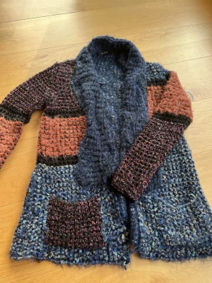 Färgglad stickad kofta från Desigual - Unik stickad kofta från Desigual i färgerna marinblå, rostbrun och svart. Koftan har en grovstickad struktur, stora fickor framtill och en bred krage. Materialet är en mix av ull och syntet, vilket ger en mysig och trendig look.