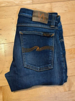 Mörkblå Nudies - Snygga mörkblå jeans från Nudie Jeans med klassisk femficksmodell. Jeansen är modell long John vilket motsvarar slim. Jeansen är tillverkade i mjukt denimtyg. Perfekta för en avslappnad och trendig stil. Pris är ej hugget i sten. Uppsydda ungefär till l28