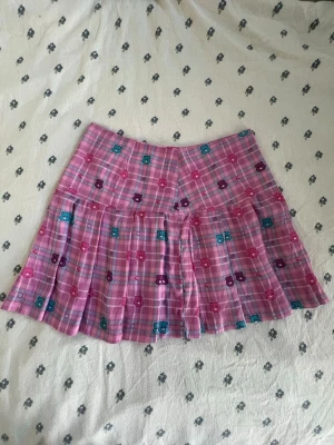 Care Bears x dolls kill rosa kortkjol - Söt care bears x dolls kill limited edition kortkjol i rosa med rutigt mönster och Krambjörnarna i rosa blått och lila. Kjolen har veckad nederdel och är perfekt för dig som gillar färgglada och lekfulla plagg. Passar till både sneakers och boots för en cool look. Storlek s. Måtten finns i bilderna. 