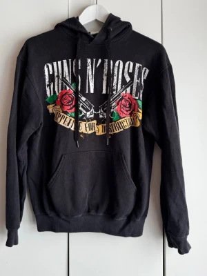 Guns N' Roses svart hoodie. S. Emp shop. - Svart hoodie med stort Guns N' Roses-tryck fram och bak, 'Appetite for Destruction'. Klassisk känguruficka och dragsko i huvan. Mjuk o go. Storlek S, Inköpt på EMP shop, Fruit of the Loom. Perfekt för dig som gillar rock och vill sticka ut. Använd en del och ytludd finns, men bra skick. Trycken hela o fina. 