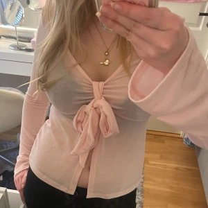 Ljusrosa topp med knyt - Säljer en ljusrosa omlottopp med lång ärm och knyt framtill. Perfekt att styla med kjol och jeans