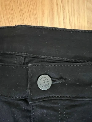 Svarta jeans från Cheap Monday - Säljer ett par svarta jeans från Cheap Monday med smal passform och klassisk femficksdesign. Jeansen har en ikonisk dödskalleknapp och raka ben. Materialet är stretchigt för extra komfort och passar perfekt till en trendig vardagslook.