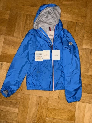 Moncler Windbreaker - Säljer en äkta ljusblå Moncler windbreaker i str 14a jag skulle säga att de passar de som är runt 152-164cm. Den är köpt på nk Göteborg för två år sedan och nypris var då runt 3799:- men nu ligger priset runt 4000:- . Nfc funkar såklart och jackan är i nyskick. Extra knappar ingår!
