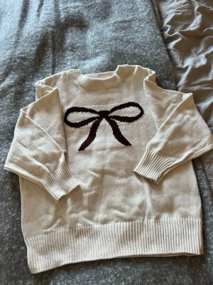 Stickad tröja från Gina Tricot  - Stickad tröja, naturvit med mörkt vinröd rosett på framsidan. Storlek 170. Använd en gång, tvättad en gång.