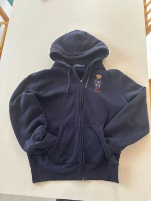 Polo Ralph Lauren Zip Hoodie - Zip från Ralph Lauren, den är i bra skick förutom att själva ”fästet” på dragkedjan borta. Dragkedjan funkar fortfarande bara att det är lite pilligt att få upp den!