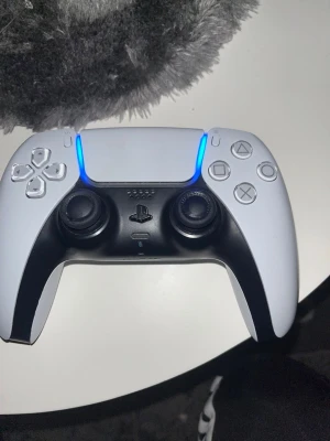 Vit och svart PS5 DualSense handkontroll - Snygg DualSense handkontroll till PlayStation 5 i vit och svart design. Ergonomisk form med två analoga spakar, touchpad, adaptiva triggers och inbyggd mikrofon. Tillverkad i plast med klassiska PlayStation-symboler på knapparna.