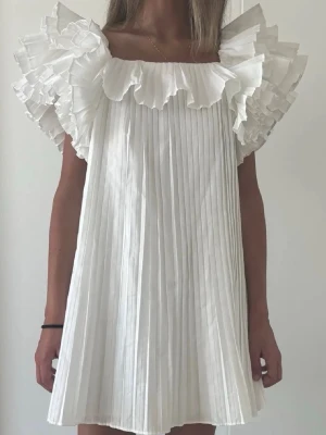 Vit plisserad kortklänning med volang - En supersöt klänning från zara i storlek xs, prislappen är kvar och den är aldrig använd! Säljer då den inte passade mig tyvärr💕