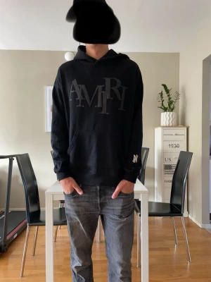 Svart hoodie från Amiri med logga - Svart hoodie från Amiri i 100% bomull med stor AMIRI-logga framtill och en mindre logga på ärmen. Klassisk huva utan snören, perfekt för en streetwear-look. Snygg och stilren design med en lite loose passform. Storlek M. Har ni några frågor så är det bara att fråga! Priset är inte hugget i sten.