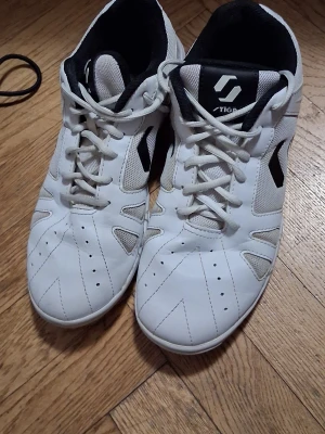 Stiga Liner IV - Säljer ett par vita inomhusskor från Stiga med svart logga på sidan och tungan. Skorna har snörning, ventilerande meshpaneler och slitstark gummisula med mönster för bra grepp. Perfekta för sporter som innebandy eller badminton. Endast använda 1 termin innomhus!