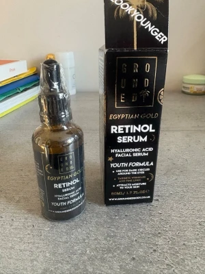 Grounded Egyptian Gold Retinol Serum - Grounded Egyptian Gold Retinol Serum med hyaluronsyra är ett ansiktsserum i en brun glasflaska med pipett. Förpackningen är svart med gulddetaljer och text. Serumet är en youth formula som hjälper mot mörka ringar, fina linjer och återfuktar huden.