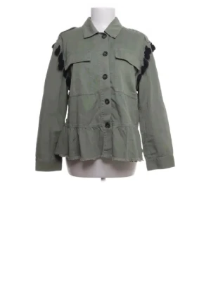 Grön jeansjacka från Zara - Grön jeansjacka från Zara med knappar framtill och volangkant nedtill. Baksidan har ett färgglatt broderat mönster med svarta tofsar längs kanterna. Jackan har lång ärm och en avslappnad passform.