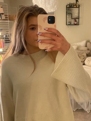 Ljusbeige oversized stickad tröja - Mysig ljusbeige stickad tröja med breda, långa ärmar och ribbade detaljer vid halsringning och ärmslut. Tröjan har en avslappnad, oversized passform och är perfekt för lager på lager. Passar dig som gillar en enkel men trendig stil.