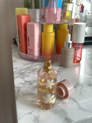 Daily Love parfym  - Säljer en söt parfym från VYONA som heter Daily Love. Flaskan är genomskinlig med vita och gula prästkragar tryckta på glaset och har ett guldigt sprayhuvud samt ett ljusrosa lock. Perfekt för dig som gillar blommiga och fräscha dofter.