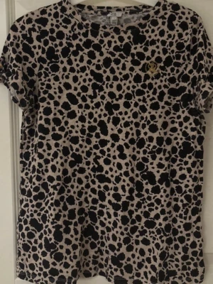 Leopardmönstrad t-shirt River Island - Snygg leopardmönstrad t-shirt från River Island i beige och svart. T-shirten har korta ärmar, rund halsringning och ett litet guldfärgat emblem på bröstet.