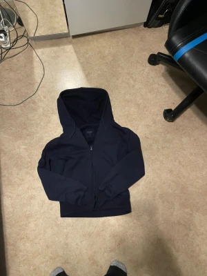 Mörkblå hoodie med dragkedja - Snygg mörkblå hoodie från H&M med dragkedja framtill och klassisk huva. Tillverkad i mjukt bomullsmaterial och har ribbade muddar vid ärmslut och nederkant. Perfekt för en avslappnad och stilren look.