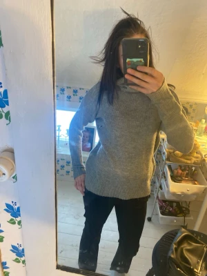 Grå polotröja i stickat material - Säljer en grå stickad polotröja med lång ärm och ribbstickad krage. Tröjan har en klassisk och enkel design som är lätt att matcha med olika outfits. Perfekt för att hålla sig varm under kyliga dagar.