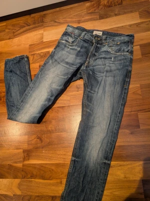 Blå Hilfiger Denim jeans straight fit - Säljer ett par klassiska blå jeans från Hilfiger Denim med snygg slitning och raka ben. Jeansen har fem fickor, normal passform och detaljerade sömmar på bakfickorna. Perfekta till sneakers och hoodie för en chill look. Om inte priset stämmer, lägg ett bud 🤗