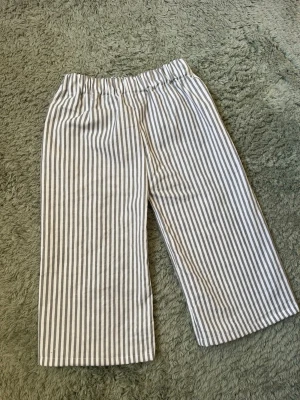 Randiga byxor med resår - Snygga handsydda byxor med vita och grå vertikala ränder och bekväm resår i midjan. Byxorna har raka ben och är tillverkade i ett lätt och luftigt material som passar perfekt för varma dagar.